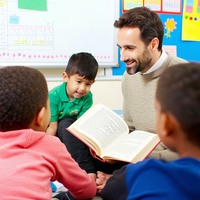 a class in key stage 1 listen to a male teacher reading alound-3